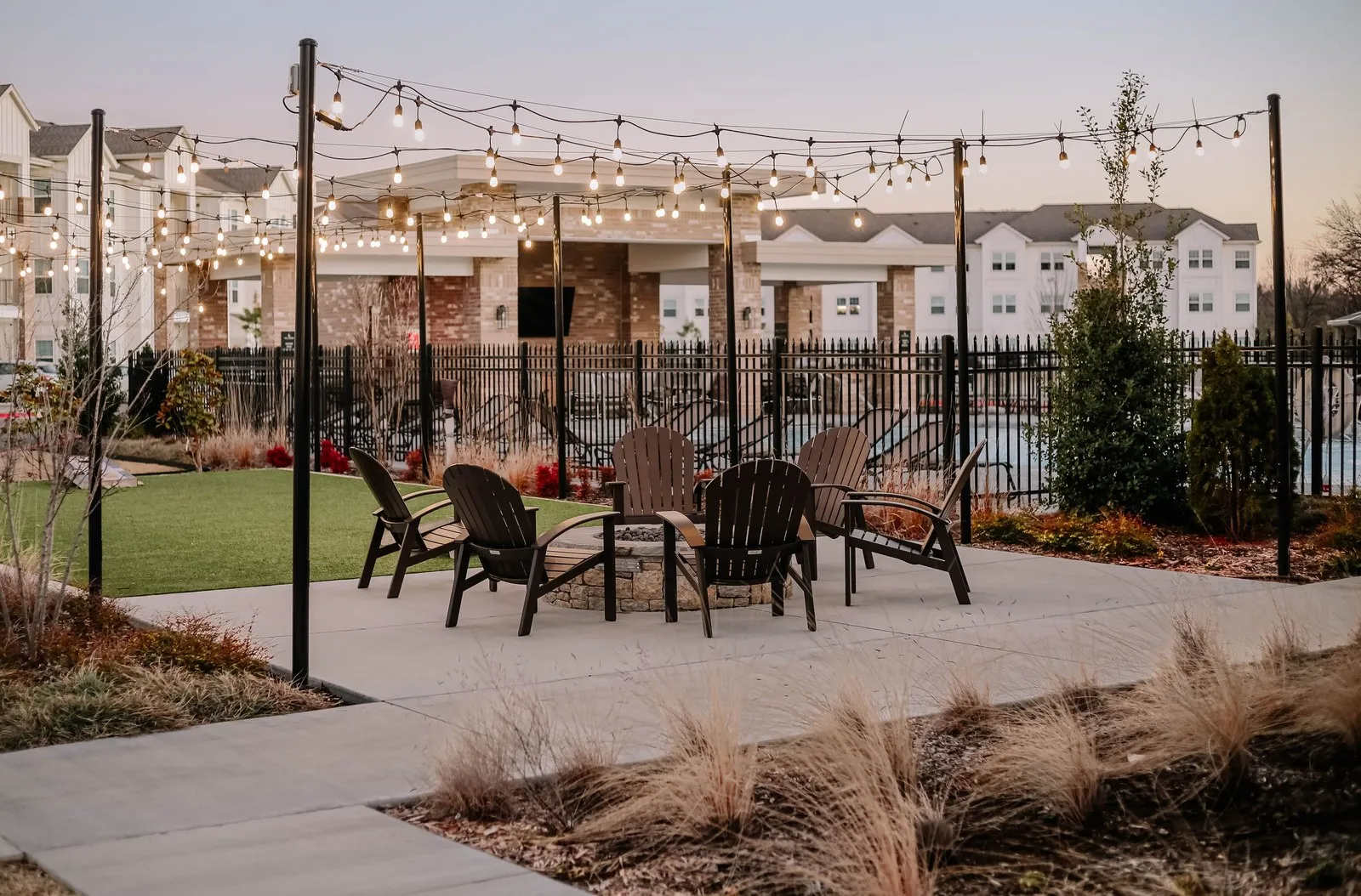 Chairs around a fire pit under a canopy of warm string lights at dusk.