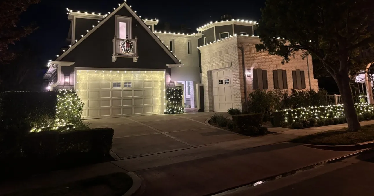 A two-story home with warm white C9 lights outlining the roofline, gables and garage door at night.